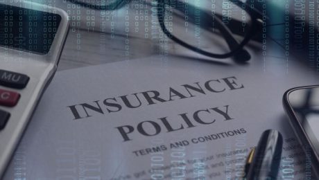 Insurance Policy on table with technology around to depict cyber insurance