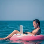 mid age man working on laptop while floating in the sea summer vacation